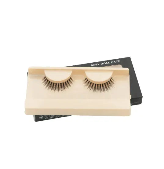 Faux cils ‘Baby Doll Gaze’ présentés sur un support beige, offrant un effet naturel et séduisant. Idéals pour un maquillage des yeux sophistiqué.