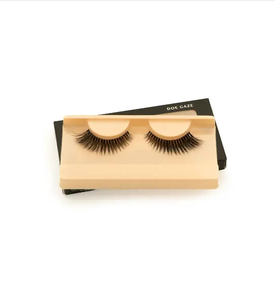FAUX CILS «DOE GAZE» présentés sur un support beige. Faux cils volumineux et sophistiqués, parfaits pour un maquillage des yeux captivant.